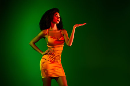 Stunning young woman showcasing confidence in a vibrant cocktail dress against a rich green backdropの写真素材