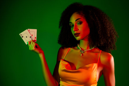 Elegant young woman in fashionable dress holding playing cards against a vibrant green backgroundの写真素材