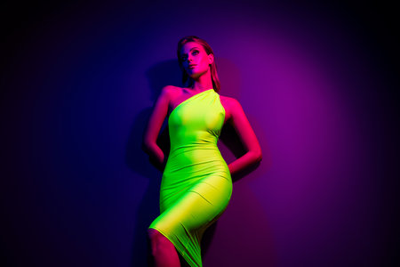 Young fashionable woman in green dress posing confidently under vibrant neon lighting in a club settingの写真素材