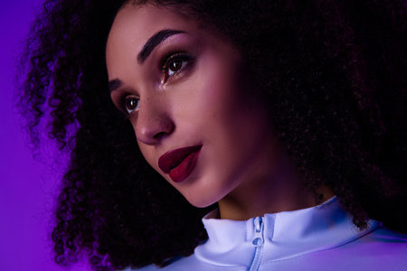 Portrait of a trendy woman with curly hair illuminated by purple neon, showcasing beauty, fashion, and cosmeticsの写真素材