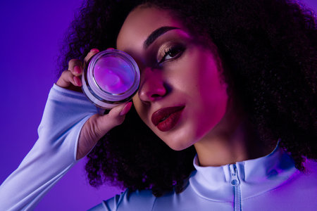 Young woman holding cosmetic product in neon light ambiance exudes glamour and styleの写真素材