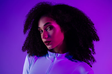 Trendy woman in a stylish jumpsuit illuminated by neon lights against a violet background, expressing beautyの写真素材