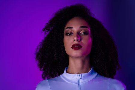 Portrait of a fashionable young woman with curly hair against a vibrant purple background, expressing styleの写真素材