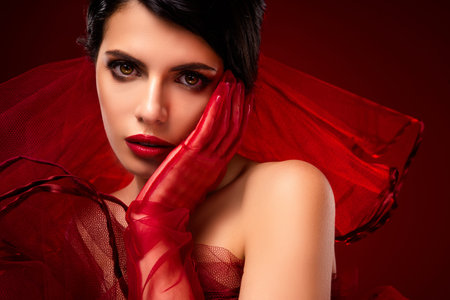 Elegant woman in stylish red attire posing gracefully with captivating look on red gradient backgroundの写真素材