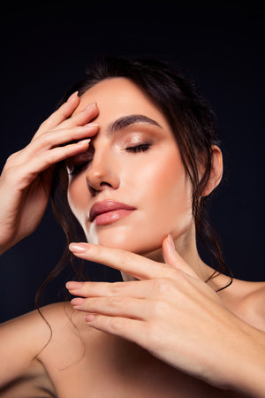 Young brunette woman with elegant makeup and hairstyle expressing sensual beauty on a dark backgroundの写真素材