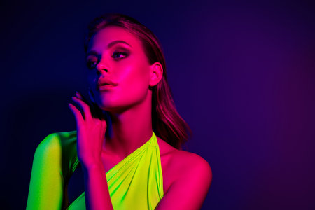Fashion portrait of a young woman with neon lights blending green and pink hues over dark backgroundの写真素材