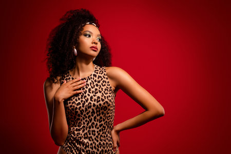 Stylish young woman in leopard print outfit with bold makeup posing against a red gradient backgroundの写真素材