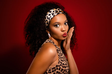 Young woman in leopard print outfit with curly hair and headband posing against red backgroundの写真素材