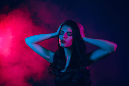 Beautiful young woman in neon light with pink and blue accents standing against a smoky background