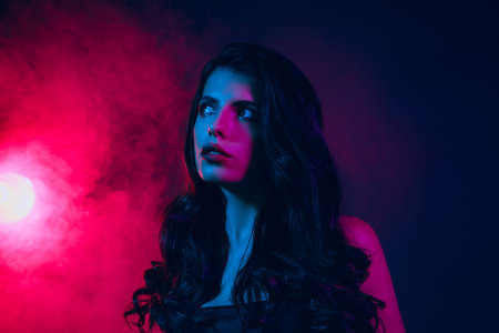 Portrait of a young woman in dramatic neon lighting with a smoky background, showcasing modern eleganceの写真素材