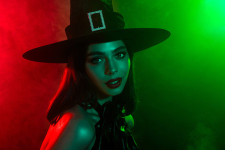 Elegant woman in witch costume amidst green and red lights during Halloween celebration