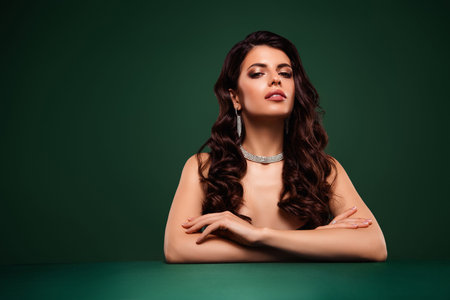 Glamorous brunette woman posing elegantly with jewelry against sleek green background.の写真素材