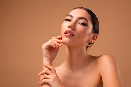 Tender portrait of a young woman highlighting beauty and style with flawless skin and a beige backgroundの写真素材