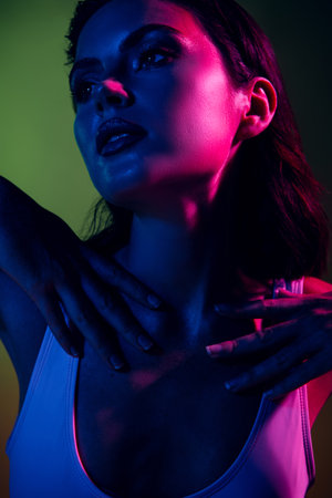Vertical portrait of a young woman with vibrant colored lighting creating a neon gradient effect under low ambient lightの写真素材