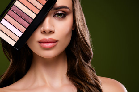 Beautiful brunette woman with elegant hairstyle and vibrant makeup holding an eyeshadow paletteの写真素材