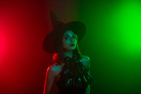 Captivating portrait of a stylish woman in a witch's hat amid vibrant Halloween-inspired lighting