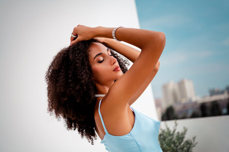Stunning young woman with curly hair posing outdoors in blue satin dress with a glamorous cityscape viewの写真素材