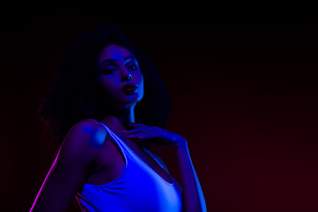 Elegant young woman in neon lighting posing confidently in stylish outfit, reflecting beauty and allureの写真素材