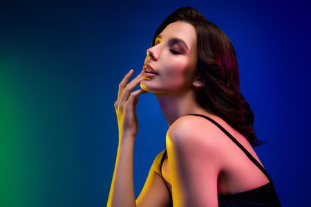 Stylish sensual brunette woman posing in neon lighting with vibrant makeup in an elegant dress showcasing beautyの写真素材