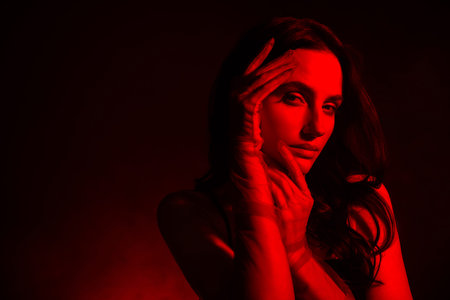 Sensual tender young woman with brunette curls and glowing red light in a stylish artistic photoshootの写真素材