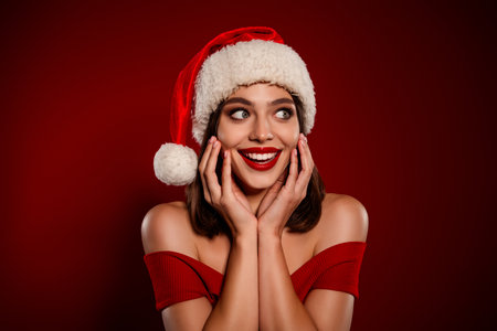Glamorous woman in Santa hat smiles with red off shoulder sweater festive christmas moodの写真素材