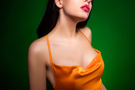 Alluring woman in vibrant orange dress with green background showcasing beauty and fashionの写真素材