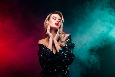Elegant blonde woman in a glamorous black sequin dress posing confidently against a smoky vibrant red backgroundの写真素材