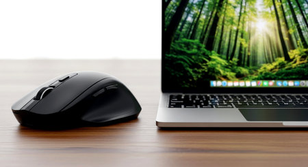 Laptop and mouse on a wooden table with a blurred nature backgroundの素材
