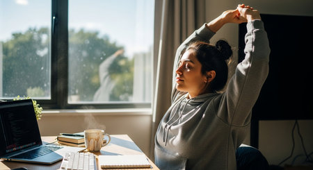 side view of tired asian woman stretching while sitting at workplace in officeの素材