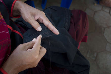 old woman's hand to picth black yarn in clothes by needleの写真素材
