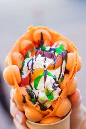 Hand holding bubble waffle with fruits, chocolate and marshmallow, with copy space.の写真素材