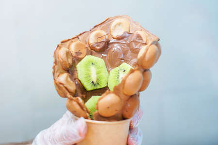 Cook prepares Hong Kong waffles with ice cream, jam and fruit. Young woman holding Hong Kong bubble wafersの写真素材