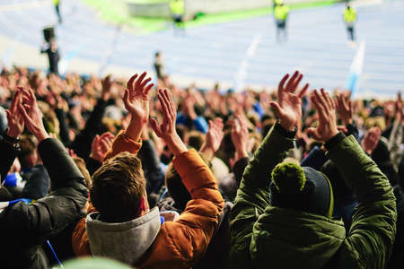 Football fans raising hands, chanting, supporting national team at stadiumの写真素材