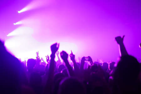 silhouettes of concert crowd in front of bright stage lightsの写真素材