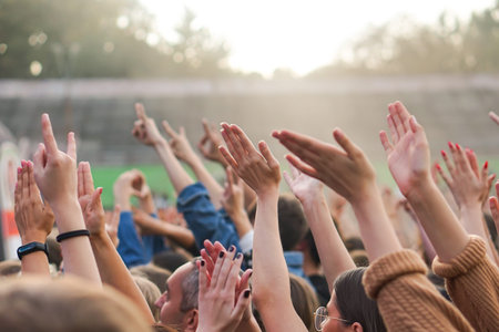 Audience with hands raised at a music festival and lights streaming down from above the stage.の写真素材