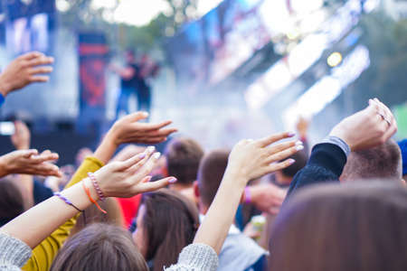 Audience with hands raised at a music festival and lights streaming down from above the stage.の写真素材