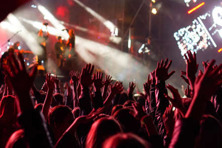 Audience with hands raised at a music festival and lights streaming down from above the stage.の写真素材