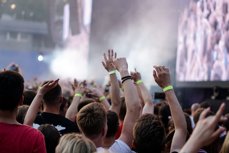 Audience with hands raised at a music festival and lights streaming down from above the stage. Soft...