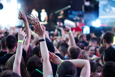 Audience with hands raised at a music festival and lights streaming down from above the stage. Soft...