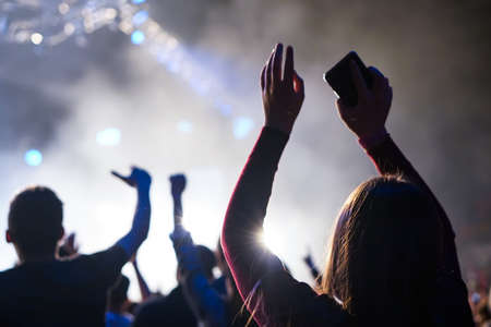 Audience with hands raised at a music festival and lights streaming down from above the stage. Soft focus, high ISO, grainy image.の写真素材