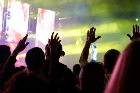 Audience with hands raised at a music festival and lights streaming down from above the stage. Soft focus, high ISO, grainy image.の写真素材