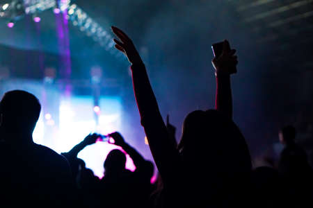 Audience with hands raised at a music festival and lights streaming down from above the stage. Soft focus, high ISO, grainy image.の写真素材