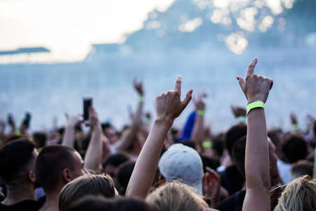 Audience with hands raised at a music festival and lights streaming down from above the stage. Soft focus, high ISO, grainy image.の写真素材