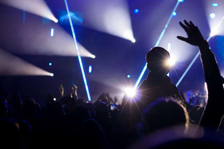 Child has fun on her parents' shoulders keeping hands with them at an outdoor rock music concertの写真素材