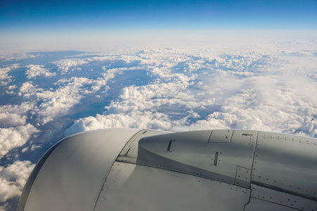 Image of wing and jet engine of airplane over blue sky.