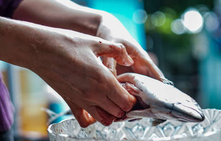 A woman cutting and cleaning fish scales off with a knife in a fish marketの写真素材