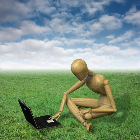 Very high resolution 3d rendering of a wooden mannequin working with his notebook sitting on the grassの写真素材