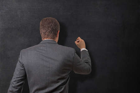 Young businessman writing on a blank blackboardの写真素材