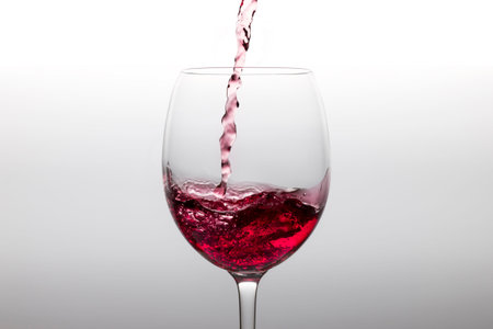 Red wine poured into a glass on a white backgorund