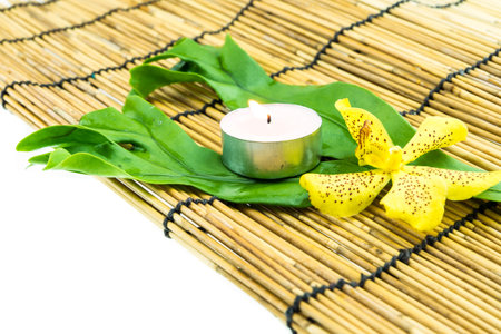 Mokkara yellow Orchid flower,green leaf and tea light candle  on bamboo backgroundの写真素材